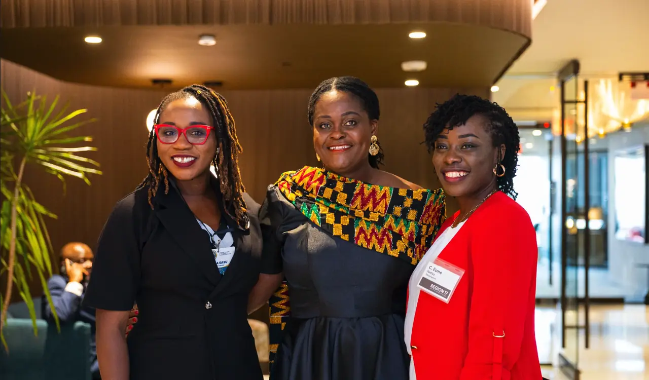 Three members standing together at the Region 17 launch, one wearing kente.